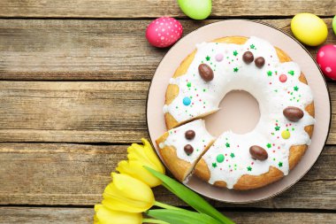 Lezzetli Paskalya pastası, boyanmış yumurtalar ve ahşap masada sarı laleler, düz yatak. Metin için boşluk
