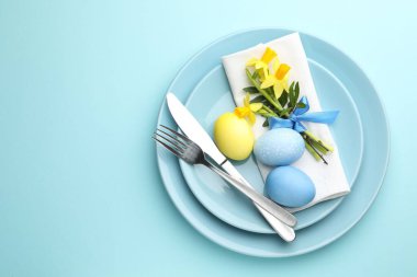 Paskalya kutlaması. Nergis çiçekleri ve açık mavi arka planda boyanmış yumurtalarla süslü masa ayarı, üst manzara. Metin için boşluk