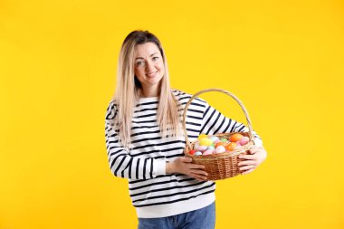 Paskalya kutlaması. Sarı arka planda boyanmış yumurta dolu sepeti olan gülümseyen kadın.