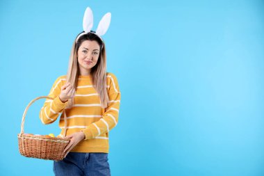 Paskalya kutlaması. Saç bandı takmış, tavşan kulaklı ve açık mavi arka planda yumurta dolu sepetli güzel bir kadın.