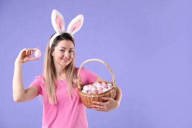 Paskalya kutlaması. Saç bandı takmış, tavşan kulaklı, menekşe arka planda boyalı yumurta dolu sepetli gülümseyen bir kadın.