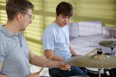 Genç çocuk içeride müzik öğretmeniyle bateri çalmayı öğreniyor.