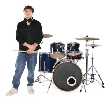 Beyaz arka planda kulaklıkları, bagetleri ve davulları olan gülümseyen genç çocuk.