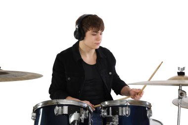 Kulaklıklı, bagetleriyle davul çalmayı öğrenen genç bir çocuk.