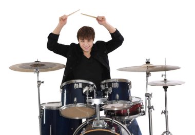 Elinde bagetlerle gülümseyen genç çocuk beyaz arka planda davul çalmayı öğreniyor.