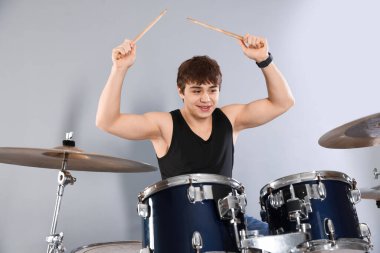 Gri arka planda davul çalmayı öğrenen güler yüzlü genç çocuk.