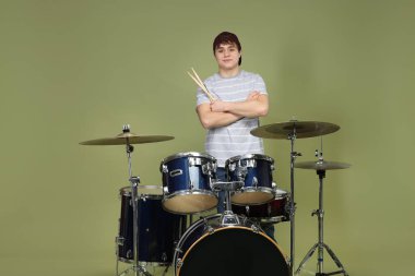 Beyzbol şapkalı, davul setiyle yeşil arka planda genç bir çocuk.