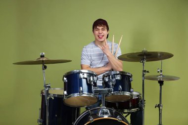 Beyzbol şapkalı ve davul seti takan genç çocuk yeşil arka planda kaya hareketi gösteriyor.