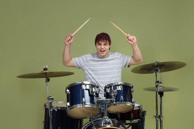 Beyzbol şapkalı gülümseyen genç, bagetleriyle yeşil arka planda davul çalmayı öğreniyor.