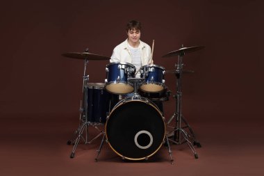 Elinde bagetlerle gülümseyen genç çocuk davul çalmayı öğreniyor.