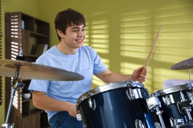 Elinde bagetlerle gülen genç çocuk içeride davul çalmayı öğreniyor