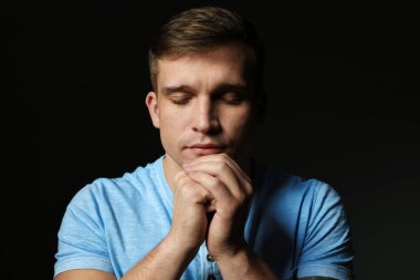 Din. Genç adam siyah arka planda dua ediyor.