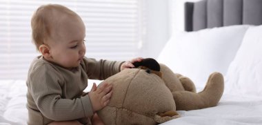 Evde yatağında oyuncak ayıyla sevimli bir bebek.