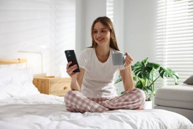 Evdeki yatakta bir fincan kahve ve akıllı telefonla güzel bir kadın.