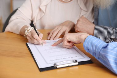 Noter, ahşap masada son arzuları ve vasiyetnameleri imzalayacakları yeri gösteriyor.