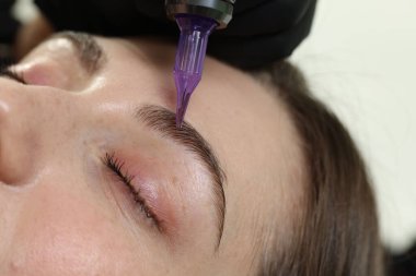 Güzellik uzmanı genç bayana kalıcı kaş makyajı yapıyor.