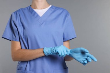 Sağlık çalışanı gri arka planda eldiven takıyor, yakın plan.