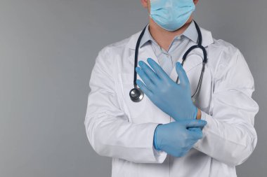 Doktor gri arka plana eldiven takıyor, yakın plan. Metin için boşluk