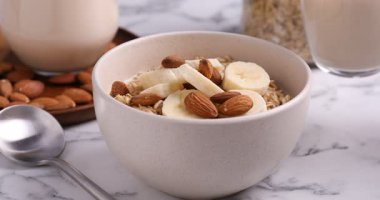 Beyaz mermer masada yulaf gevreği, muz ve fındıklı badem sütü kaseye boşaltılıyor.