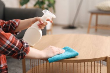 Elinde temizlik malzemesi olan bir kadın ahşap masadaki tozu temizliyor, yakın plan.