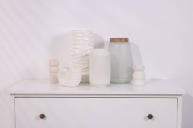 Açık duvarın yanındaki beyaz çekmecelerde bir sürü şık vazo var.