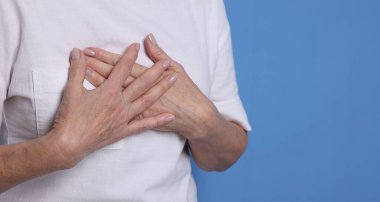 Kalp krizi geçirdi. Mavi arka planda göğüs ağrısı çeken son sınıf öğrencisi kadın, yakın plan. Metin için boşluk