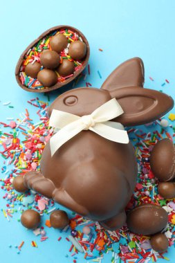 Çikolatalı Paskalya tavşanı, şekerli yumurta ve açık mavi arka planda serpiştirilmiş şeker, düz uzanmış