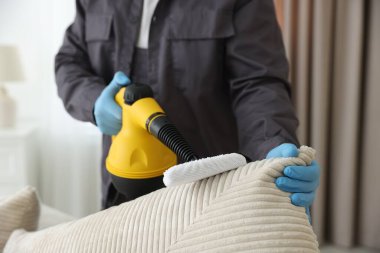 Haşere kontrol işçisi kanepeyi temizliyor. Kapalı alanda buhar temizleyicisi var.