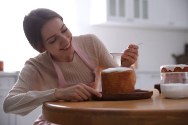 Genç bir kadın geleneksel paskalya pastasını mutfakta jöleli dekore ediyor.