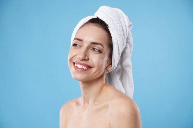 Saçları açık mavi arka planda havluya sarılı güzel bir kadın.