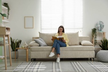 Dergisi olan kadın evinde kanepenin yanında dinleniyor.