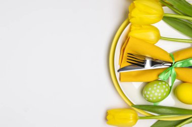 Paskalya kutlaması. Beyaz arka planda lale çiçekleri ve boyanmış yumurtalarla süslü masa ayarı, üst manzara. Metin için boşluk