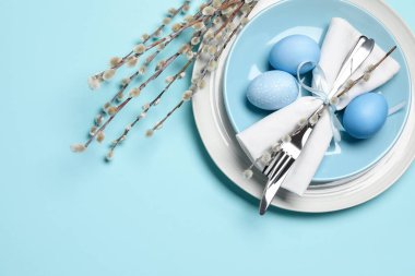 Easter celebration. Festive table setting with willow branches and painted eggs on light blue background, flat lay. Space for text