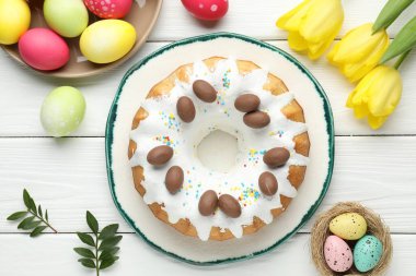 Lezzetli Paskalya pastası, boyanmış yumurtalar, sarı laleler ve yeşil yapraklar beyaz ahşap masada, düz yatıyordu.