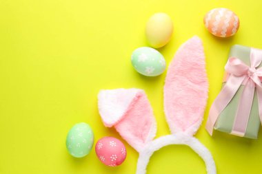 Boyalı Paskalya yumurtaları, tavşan kulaklığı ve açık yeşil arka planda hediye, düz yatak. Metin için boşluk