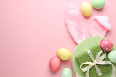 Boyalı Paskalya yumurtaları, tavşan kulaklığı ve pembe arka planda hediye, düz yatak. Metin için boşluk