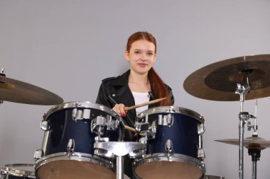 Açık gri arka planda bagetleri ve davulları olan genç bir kız.