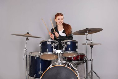 Açık gri arka planda bagetleri ve davulları olan genç bir kız.