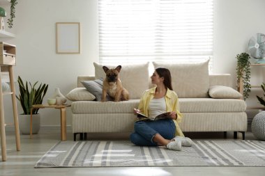 Şirin köpeği ve dergisiyle evdeki kanepenin yanında dinlenen bir kadın.