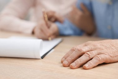 Ahşap masada son arzuları ve vasiyetnameleri imzalayan yaşlı çift, yakın plan.