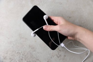 Açık gri masada akıllı telefonu ve kulaklığı olan bir kadın.