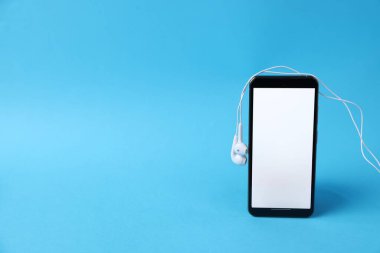 Açık mavi arka planda kulaklıklı akıllı telefon, yakın plan. Metin için boşluk