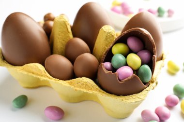 Beyaz arka planda karton çikolatalı yumurta ve şekerler, yakın plan.