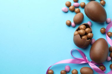 Çikolatalı Paskalya yumurtaları ve açık mavi arka planda menekşe kurdelesi. Metin için boşluk
