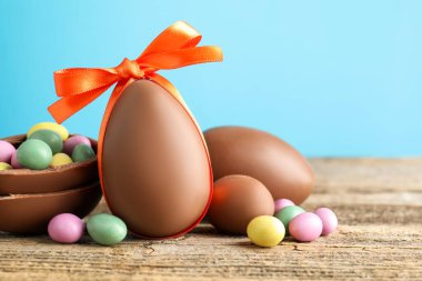 Ahşap masanın üzerinde renkli şekerlemeli lezzetli çikolata yumurtaları açık mavi arka planda, yakın plan. Mutlu Paskalyalar