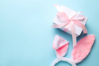 Mutlu Paskalyalar. Şirin tavşan kulakları ve açık mavi arka planda hediye kutusu, düz yatış. Metin için boşluk