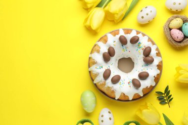 Lezzetli Paskalya pastası, boyanmış yumurtalar, lale çiçekleri ve sarı arka planda yeşil yapraklar. Metin için boşluk