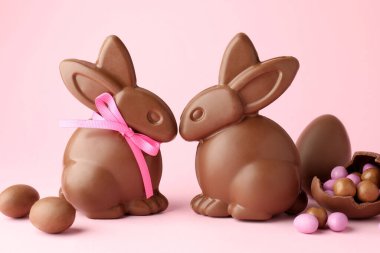 Çikolatalı Paskalya tavşanları ve pembe arka planda şekerli yumurtalar, yakın plan.