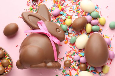 Çikolatalı Paskalya tavşanı, yumurtalar, şekerler ve pembe arka planda serpiştirilmiş şekerler.