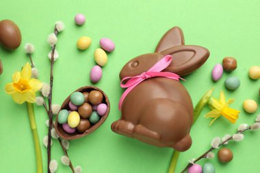 Çikolatalı Paskalya tavşanı, söğüt dalları ve açık yeşil arka planda yumurtalar, düz uzanmış.